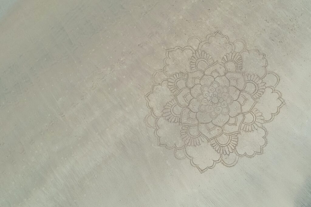 a large mandala painted on the sand on the ocean shore.
